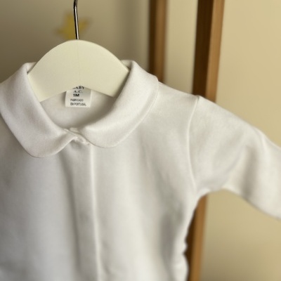 Body branco com gola redonda pendurado em cabide branco numa estrutura de madeira.