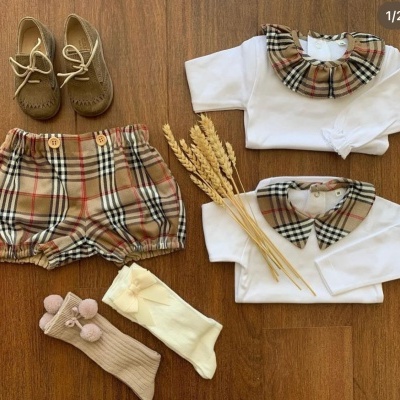 Conjunto de roupa de bebé com padrão xadrez e sapatos castanhos sobre fundo de madeira.
