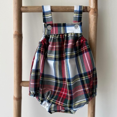 Macacão bebé xadrez tartan colorido com alças e botões, pendurado em escada de madeira