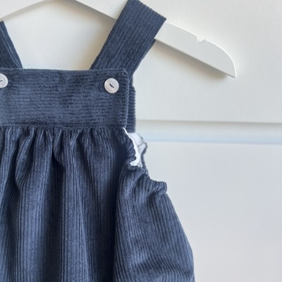 Macacão curto de veludo cotelê cinza para criança com botões brancos, pendurado num cabide branco