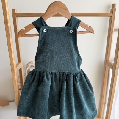 Vestido de criança verde azul escuro de veludo cotelê pendurado em cabide de madeira.