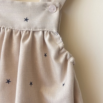 Vestido de criança bege com estrelas pretas e alças largas com botão branco