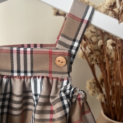 Vestido ou top infantil xadrez bege com botão de madeira e flores secas num vaso