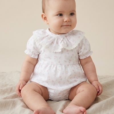 bebé com body branco estampado sentado sobre tecido neutro