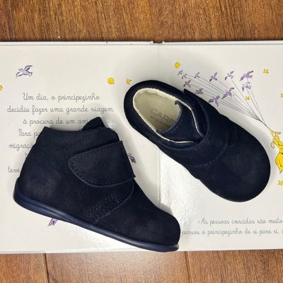 Sapatinhos pretos de bebé em camurça com velcro sobre livro aberto infantil