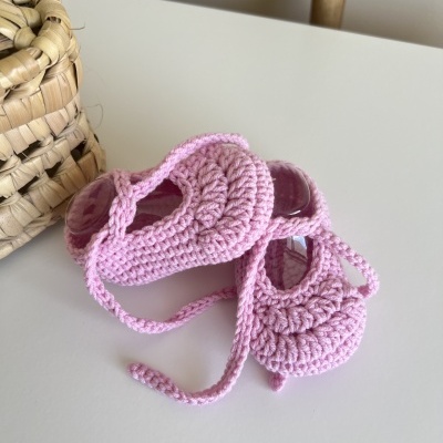 Sapatilhas de bebé cor-de-rosa em malha grossa numa superfície branca ao lado de um cesto de palha