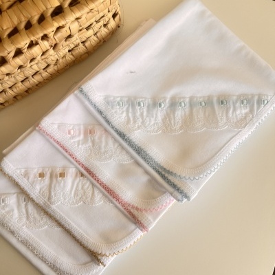 Quatro lenços brancos com bordados coloridos e renda ao lado de cesta trançada