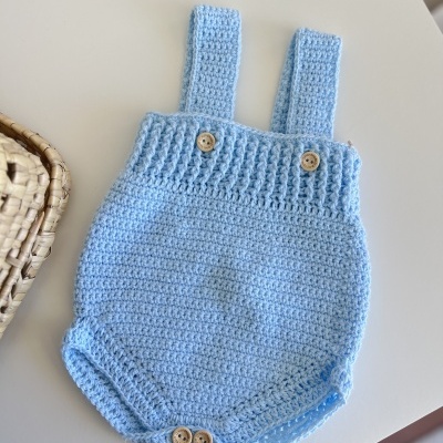 Macacão bebé azul claro croché com botões de madeira sobre superfície branca