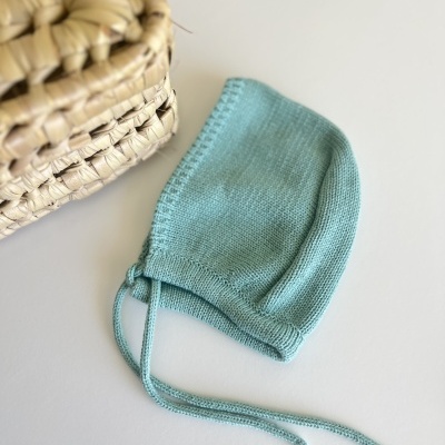 Gorro azul claro de malha para bebé com cordões ao lado de cesta trançada