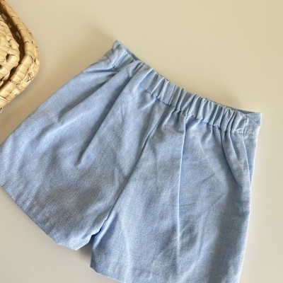 Calções azuis claros com elástico na cintura ao lado de um cesto de palha