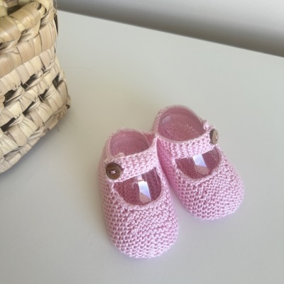 Sapatinhos de bebé cor de rosa em malha com botão castanho ao lado de cesto trançado
