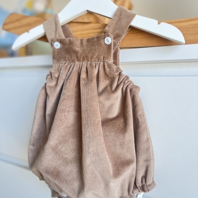 Macacão de bebé em veludo cotelê castanho claro com botões brancos pendurado em cabide branco