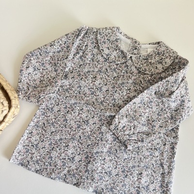 Blusa floral de criança com gola redonda e mangas compridas sobre superfície branca