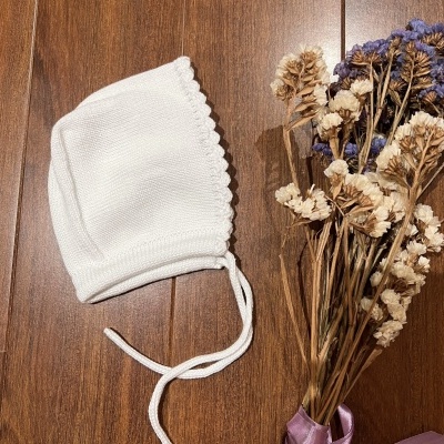 Gorro branco de malha para bebé com flores secas ao lado sobre madeira