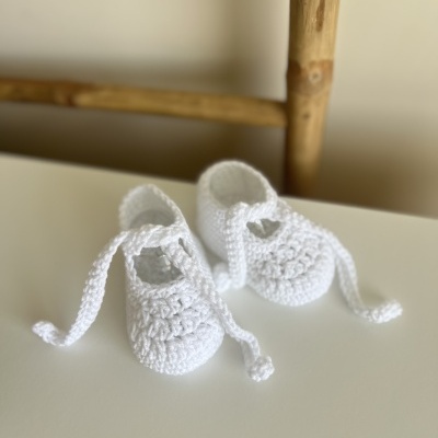 Par de sapatinhos de bebé branco em croché sobre superfície branca