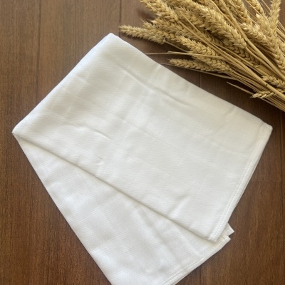 Toalha branca dobrada numa mesa de madeira com ramo de espigas secas ao lado