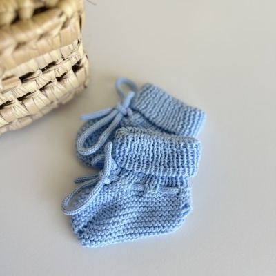 Botins de bebé tricotados azuis com cordões ao lado de um cesto de fibras naturais