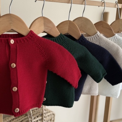 Casacos de malha para bebé em cores variadas pendurados em cabides de madeira