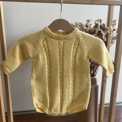 Body de bebê amarelo tricotado com padrão de trança pendurado em cabide de madeira