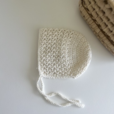 Gorro de bebé branco em croché com fitas para amarrar junto a uma cesta de vime