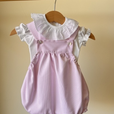 Macacão rosa e branco para bebé pendurado em cabide de madeira