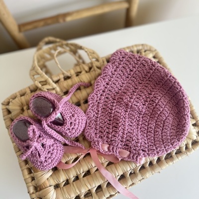 Conjunto de chapéu e sapatos de bebé em croché rosa sobre mala de palha.