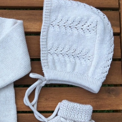 Conjunto de roupa de bebé cinzenta clara em malha com padrão trançado, sobre mesa de madeira