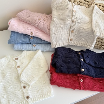 Casacos de malha infantil coloridos com botões de madeira sobre mesa branca