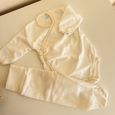 Conjunto de roupa de bebé branco com calças e camisa, sobre uma mesa branca