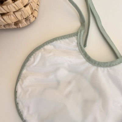 Babete branco com bordas verdes e cesto de palha ao lado