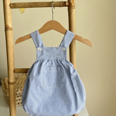 Macacão bebé azul claro riscas brancas pendurado em cabide de madeira numa escada de madeira.