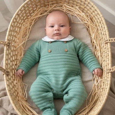 Bebé deitado numa cesta de verga com macacão verde e colarinho branco.