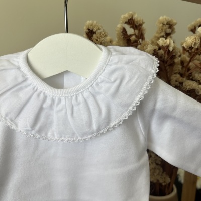 Camisola branca de bebé com gola redonda e renda pendurada num cabide