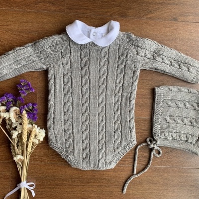Conjunto infantil de malha cinzenta com gola branca e bonnet à frente, em bancada de madeira com flores secas.