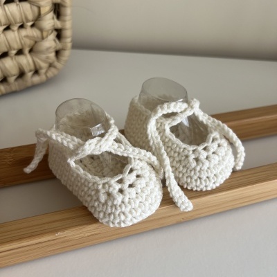 Sapatinhos de bebé brancos em malha com cadarços sobre superfície branca e espelho com moldura de madeira