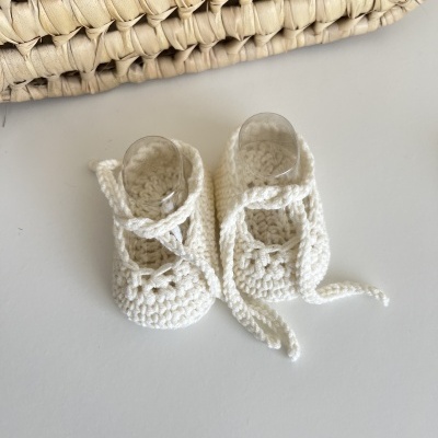 Sapatinhos de bebé em croché branco com cadarços sobre fundo branco próximo de palha entrelaçada