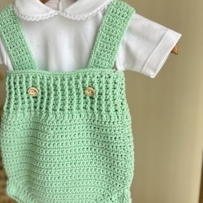Body branco com jardineira verde claro em crochet, colocado num cabide de madeira