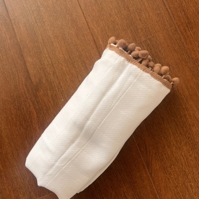 Manga de tecido branco com pompons castanhos sobre chão de madeira castanha