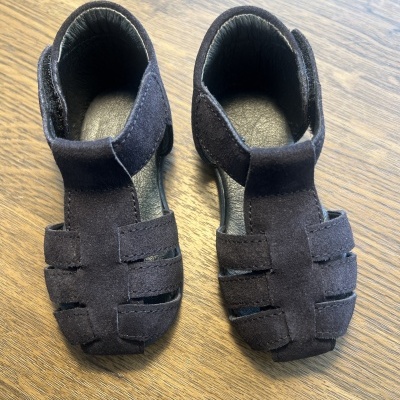 Sandálias pretas para bebé com tiras largas e fecho de velcro sobre madeira