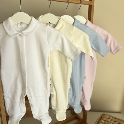 Macacões de bebé nas cores branco, amarelo claro, azul e rosa pendurados em cabides.