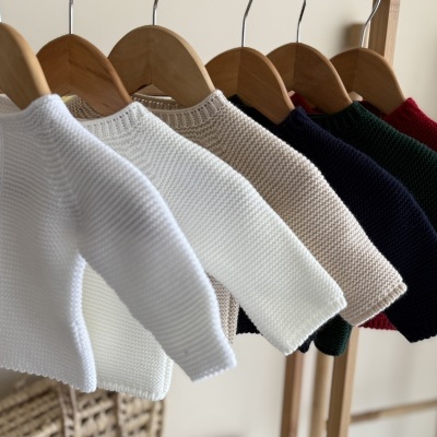 Casacos de malha coloridos para bebé pendurados em cabides de madeira.