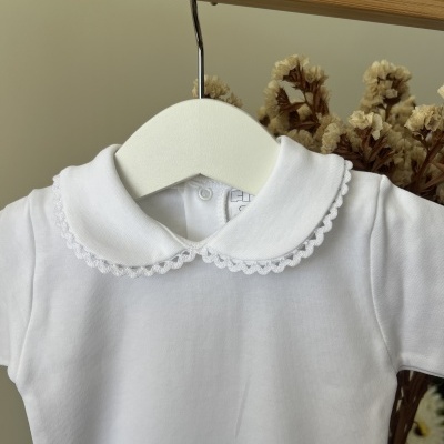Camisola branca para bebé com gola redonda decorativa e manga curta pendurada num cabide branco