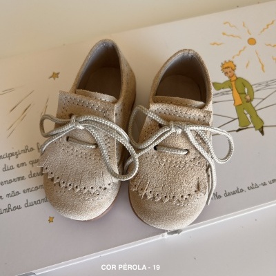 Sapatos infantis cor pérola com atacadores brancos sobre superfície com ilustração e texto