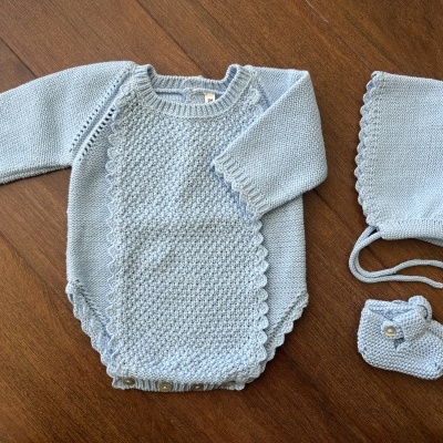 Conjunto de bebé azul claro em malha com body, touca e sapatinho sobre mesa de madeira