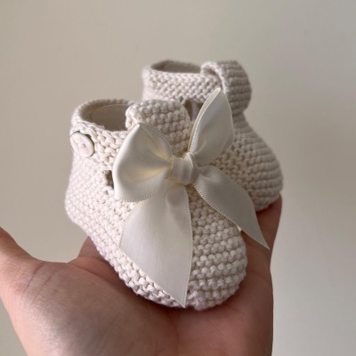 Sapatinhos de bebé tricotados creme com laço branco numa mão