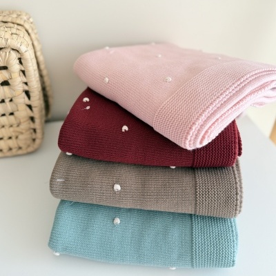 quatro mantas dobradas com pontos brancos em cores pastel empilhadas ao lado de cesto de palha