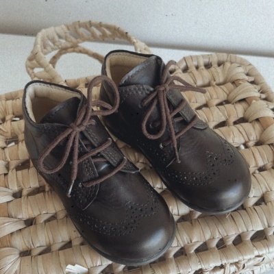 Sapatos infantis de couro castanhos sobre mala trançada bege