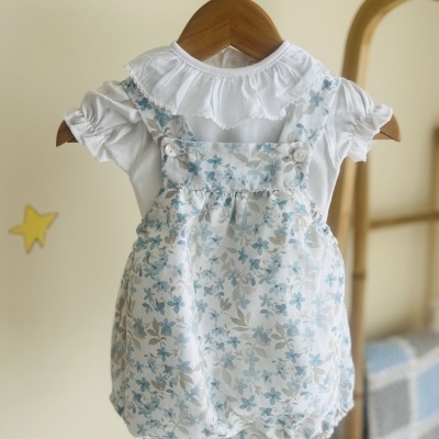 Conjunto de roupa de bebé com jardineira floral azul e body branco com folho no pescoço