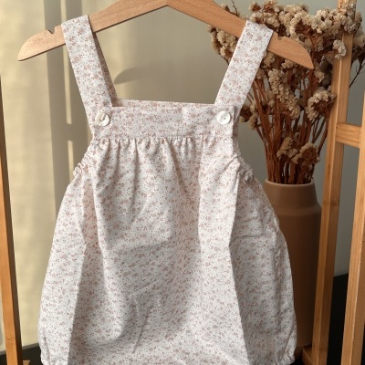 Macacão de bebé branco com flores cor-de-rosa pendurado num cabide de madeira