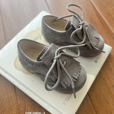 Sapatos infantis cinza em camurça com atacadores e franjas sobre caixa branca